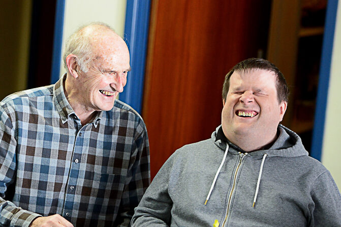 Photo shows 2 men laughing together, one is sighted and one is visually impaired and they are attending the LLBS men's group.